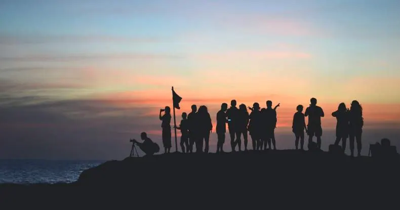 Silhuetas de um grupo de pessoas em um morro, com o pôr do sol ao fundo.