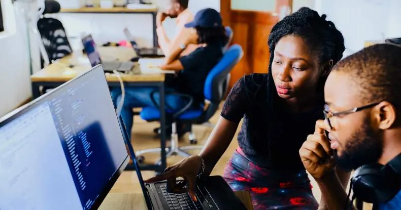 Dois colegas de trabalho colaborando em um laptop em um escritório.