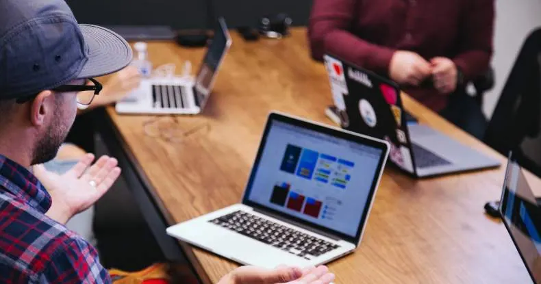 Pessoas em uma mesa de madeira com laptops abertos, discutindo ideias.