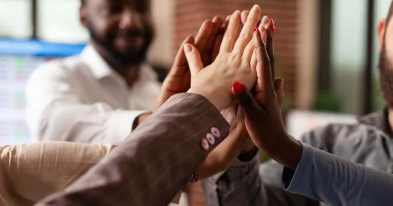 Mãos de pessoas diversas se juntando em um gesto de união e trabalho em equipe.