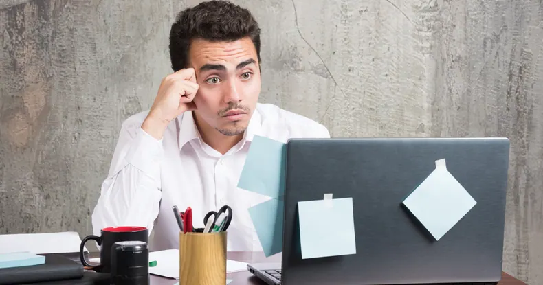 Homem de camisa branca olhando fixamente para a tela do laptop com notas adesivas.