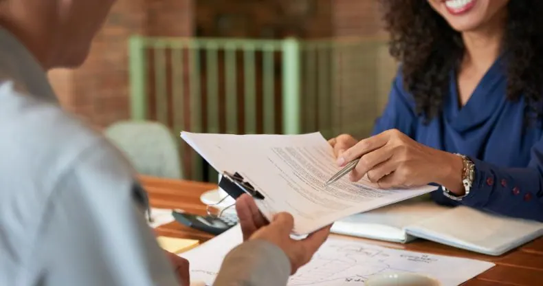 Duas pessoas revisando um documento em uma mesa de madeira.