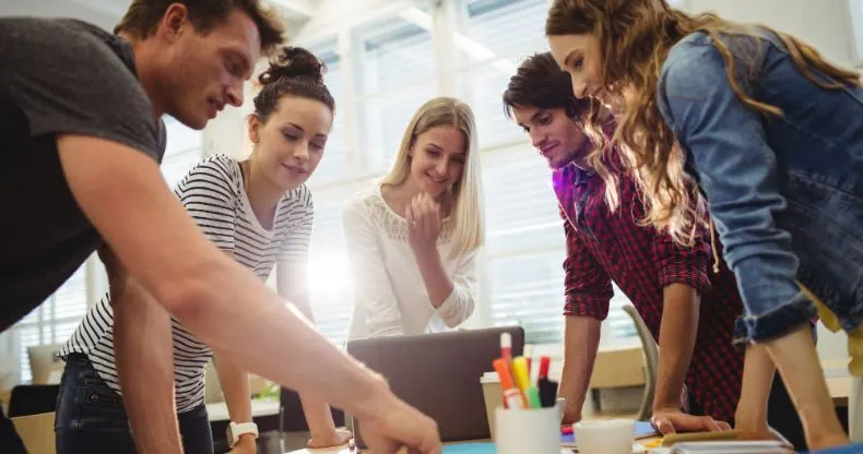 Grupo de cinco jovens profissionais olhando para um laptop em uma mesa.