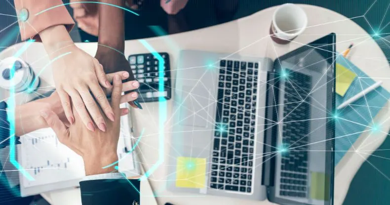 Mãos de pessoas de diferentes etnias juntas sobre uma mesa com laptops e anotações.