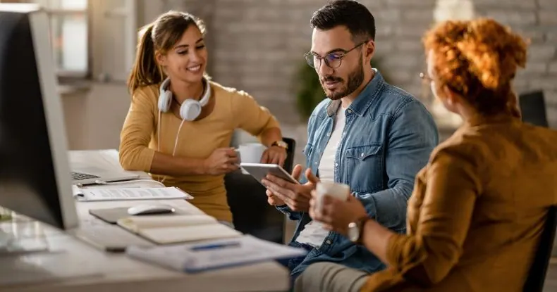 Três colegas de trabalho conversando e interagindo em um escritório moderno.