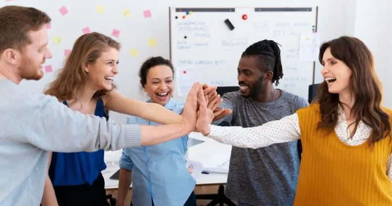 Cinco colegas de trabalho sorrindo e batendo as mãos em um escritório.