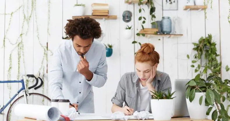 Dois colegas de trabalho, um homem e uma mulher, concentrados em suas tarefas na mesa.