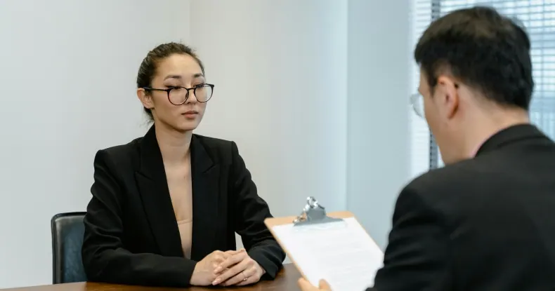 Mulher asiática de óculos e blazer preto em entrevista de emprego.