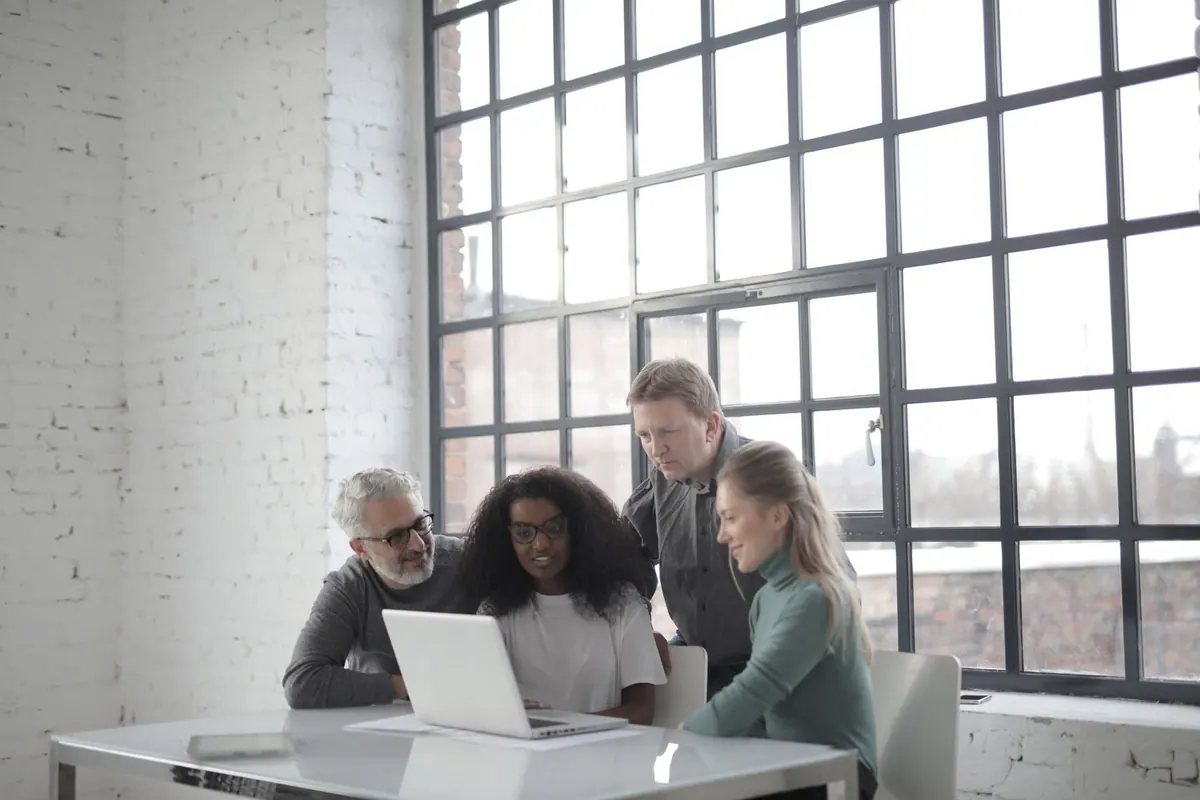 Colegas de diversas idades e etnias colaborando em torno de um laptop no escritório.