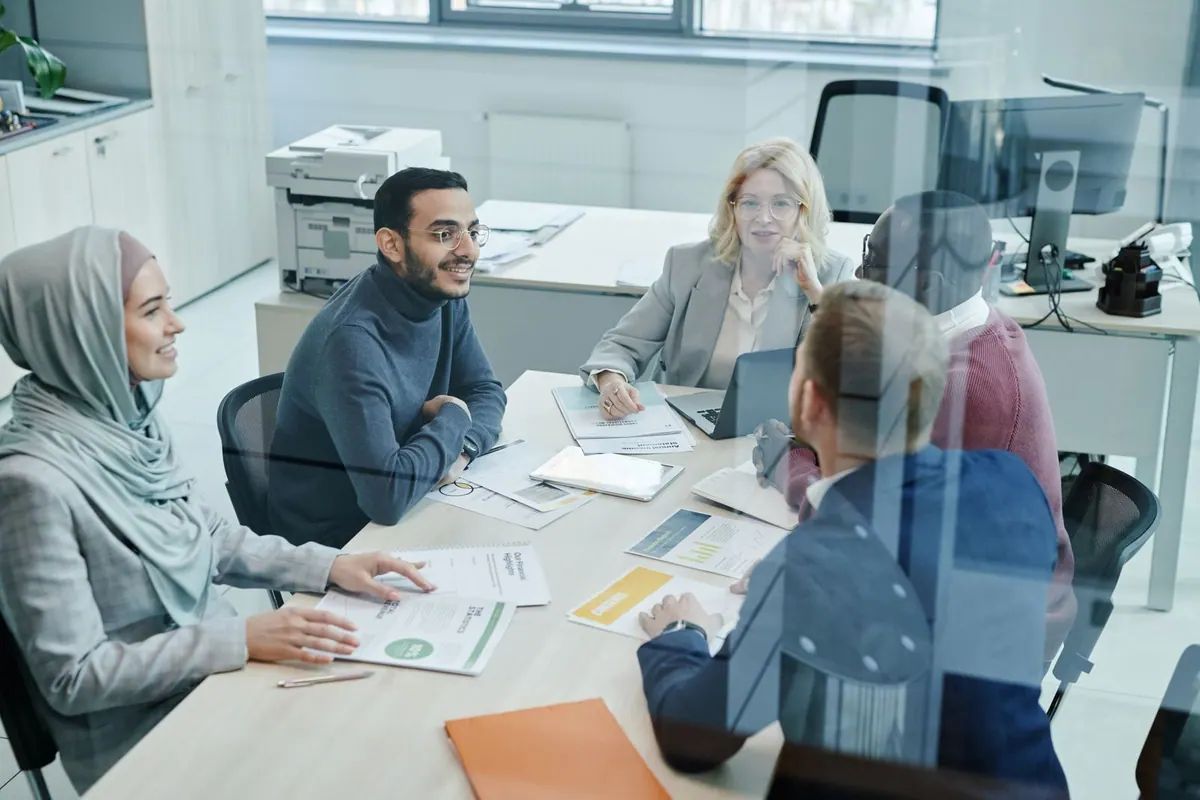 Pessoas diversas em reunião de trabalho, discutindo e aprendendo juntas.