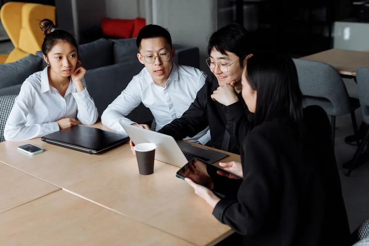 Grupo de pessoas em reunião de trabalho, olhando para um laptop e discutindo.
