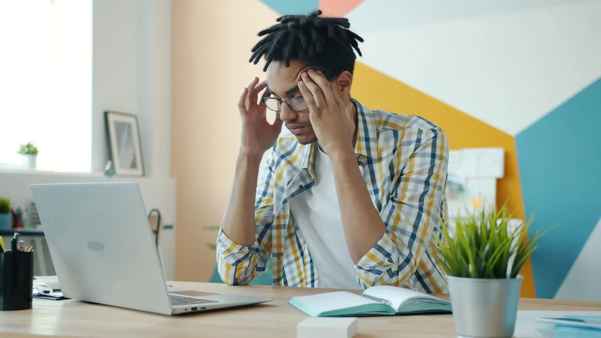 Profissional de RH estressado no escritório com laptop, refletindo sobre desafios.