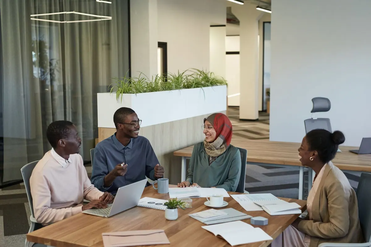 Colegas diversos sorrindo e conversando em uma mesa de reunião no escritório.