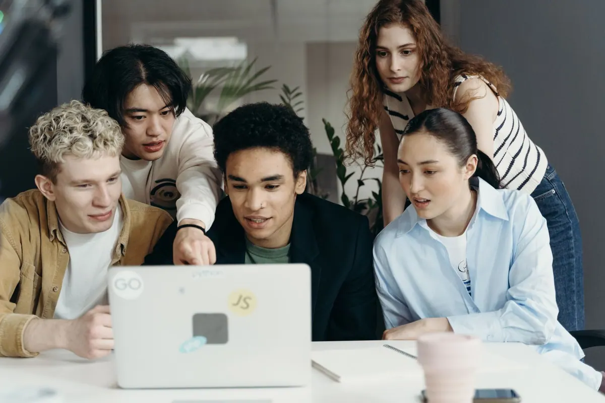 Jovens adultos diversos olhando para um laptop em um ambiente de trabalho.