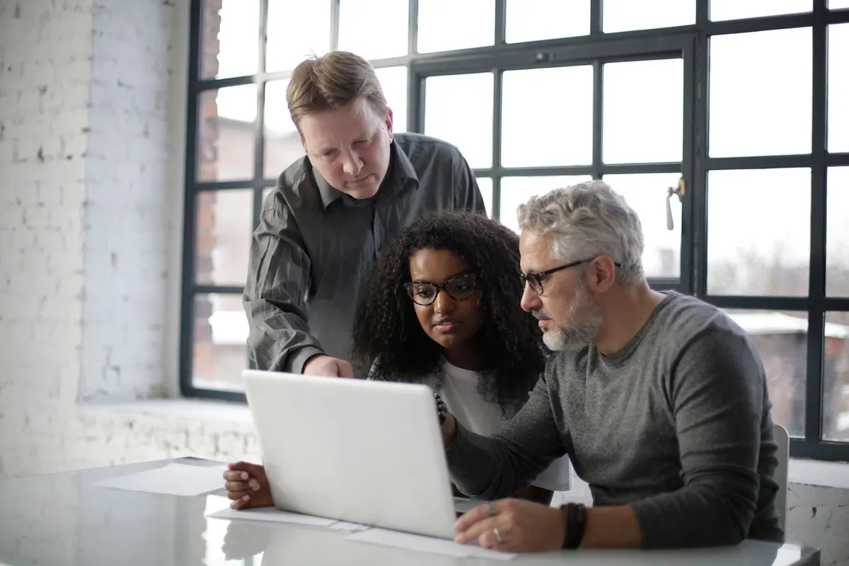 Três colegas de trabalho diversos colaborando em um laptop, focados na tela.