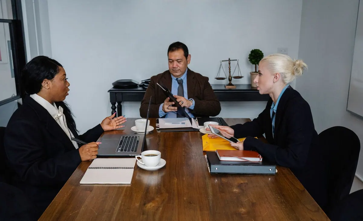 Pessoas em uma reunião de negócios, com um homem no centro e duas mulheres nas laterais.