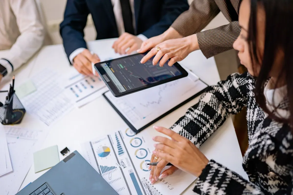 Pessoas analisando dados em um tablet durante uma reunião de trabalho.