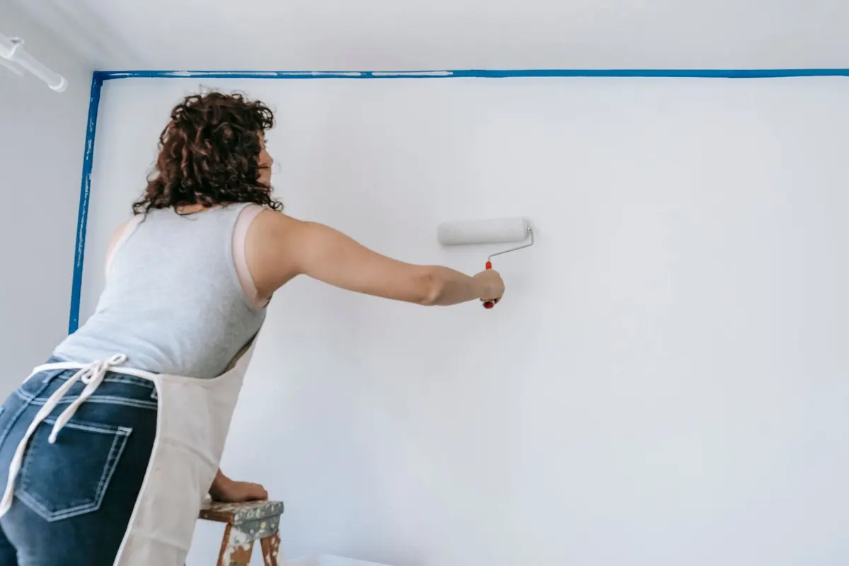 Mulher pintando uma parede com rolo, representando capacitação profissional.