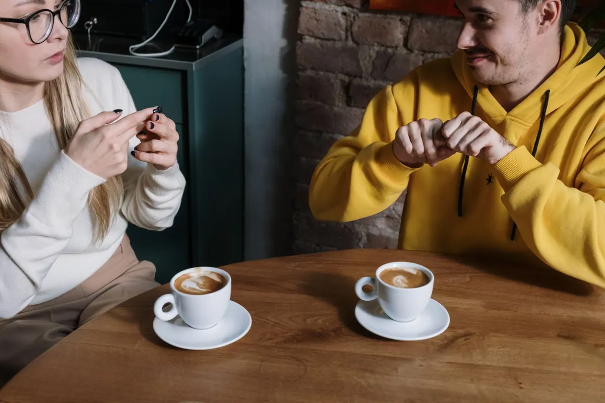 Duas pessoas conversando em língua de sinais à mesa de um café