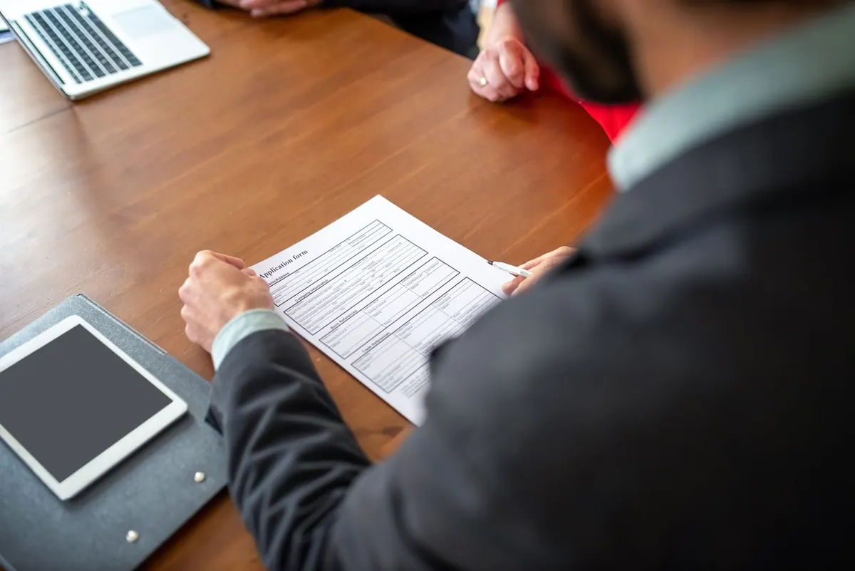 Homem lendo um formulário de candidatura em uma mesa de escritório.
