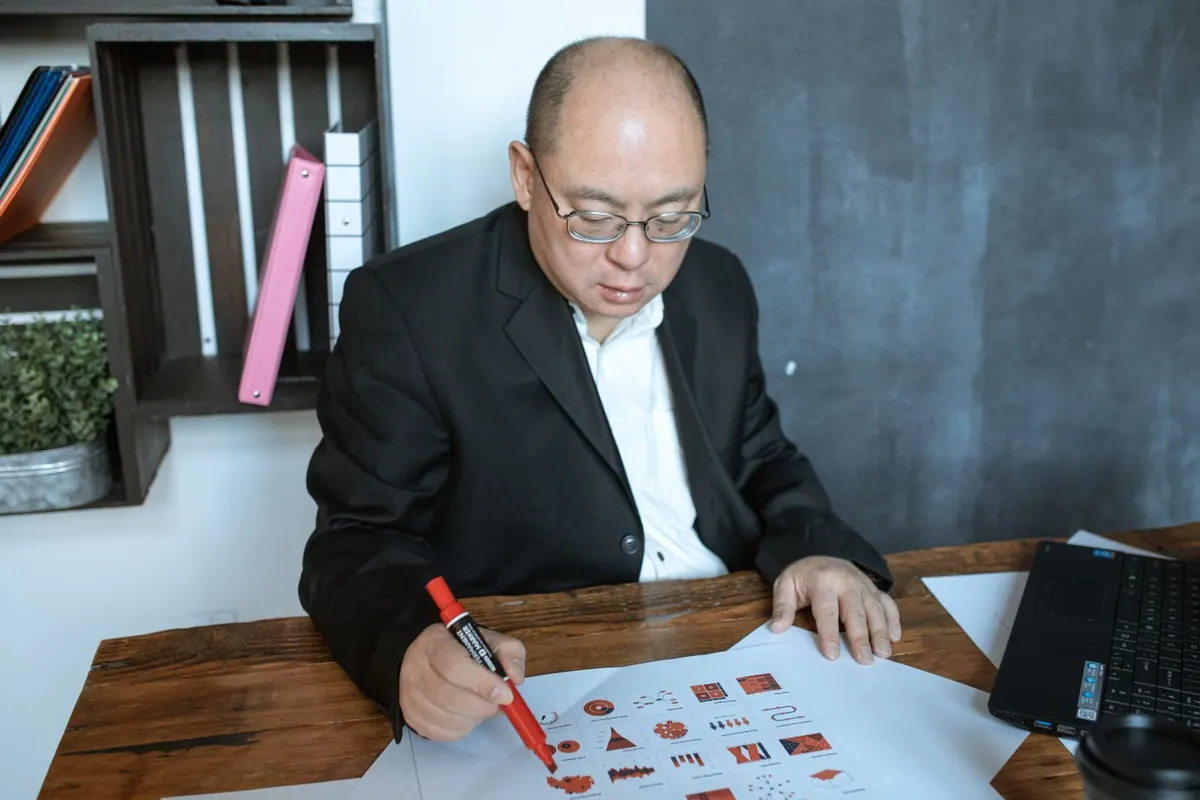 Homem de óculos analisando gráficos em papel com caneta marca-texto vermelha.