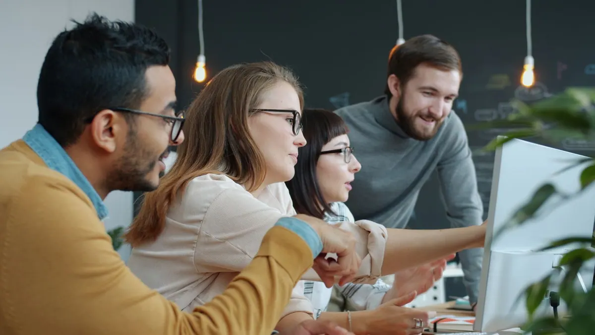 Equipe diversa de profissionais de tecnologia colaborando em frente a um monitor de computador.