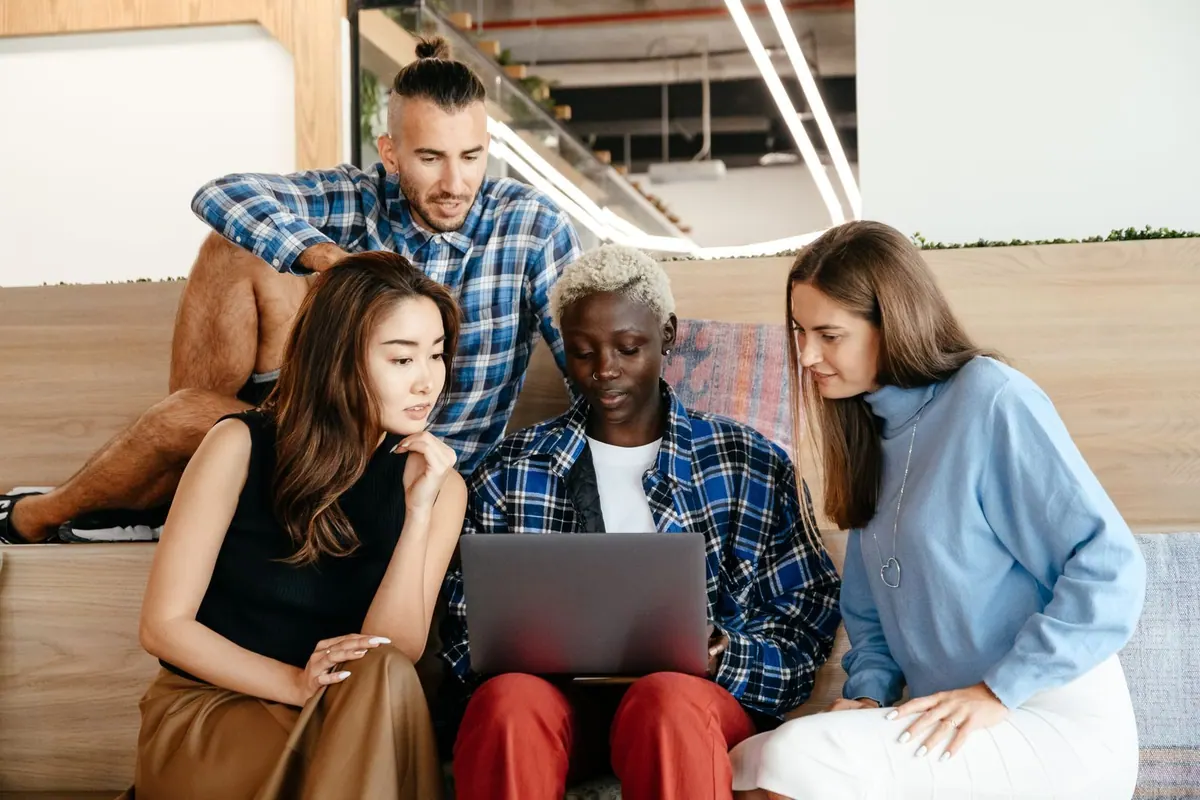 Grupo diverso de colegas de trabalho interagindo e usando um laptop em um ambiente de escritório moderno.