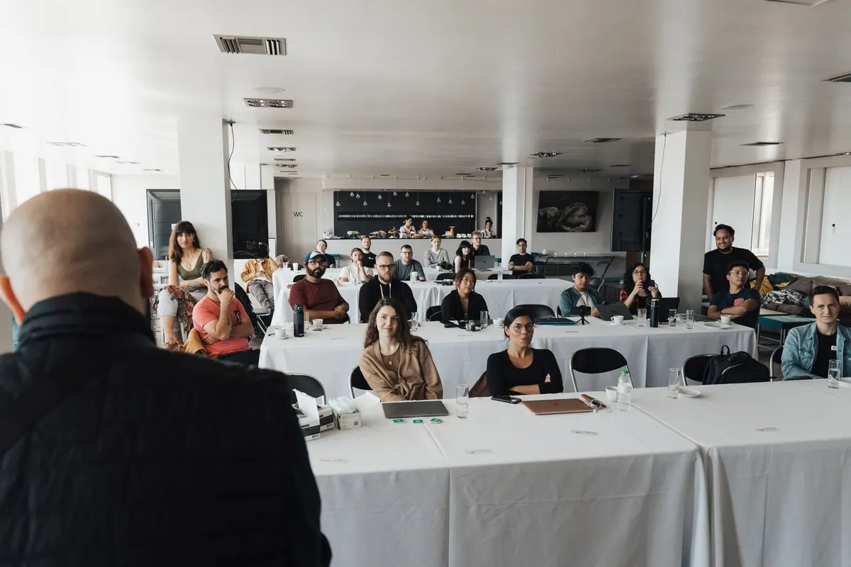 Pessoas em uma sala de treinamento, com um palestrante de costas para a câmera.