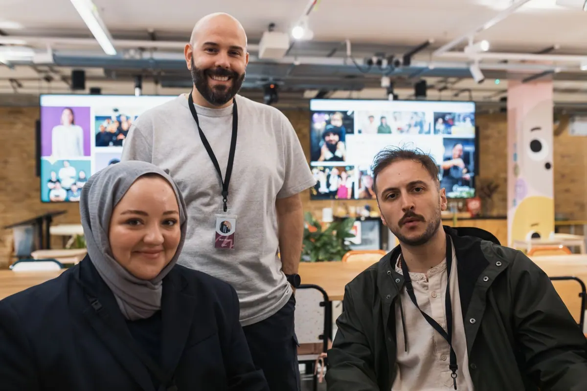 Equipe diversa em um espaço de trabalho colaborativo com telas de videochamada ao fundo.