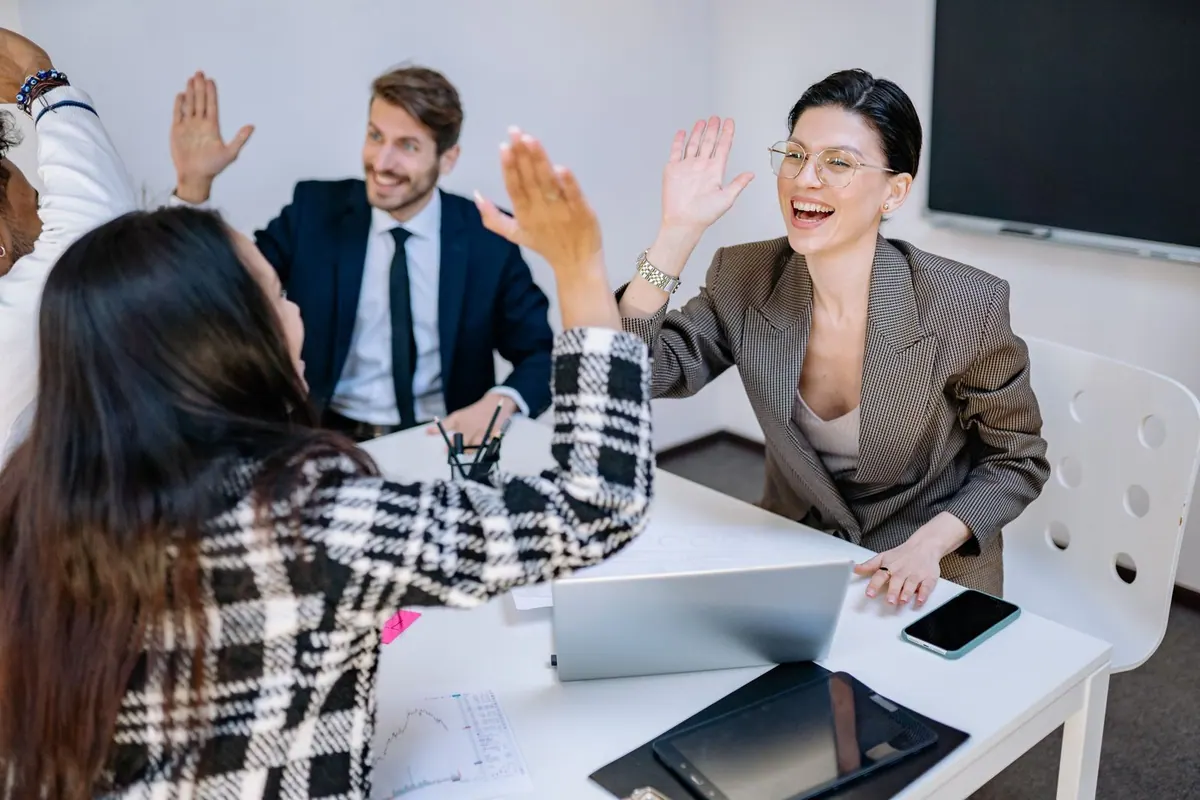 Equipe de trabalho diversa celebrando com high-five em uma sala de reunião.