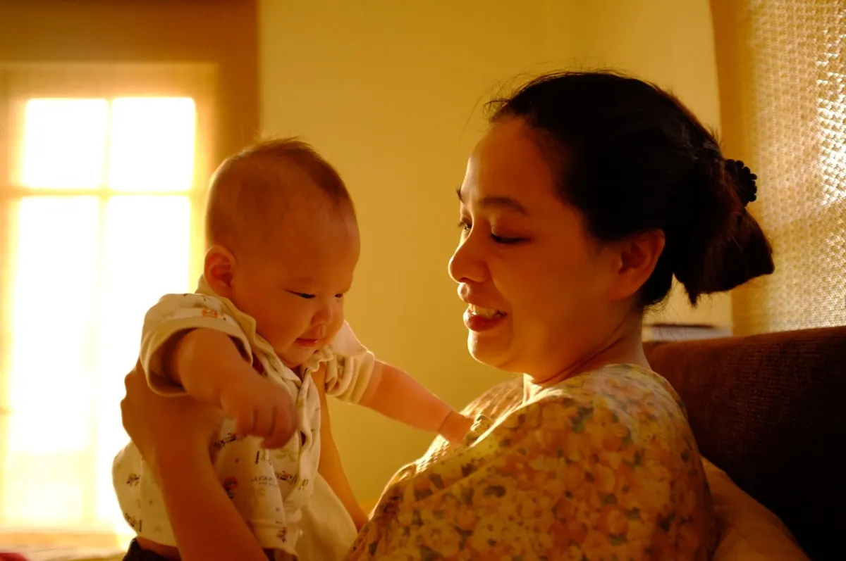 Mãe sorrindo, segurando seu bebê em casa, luz natural.