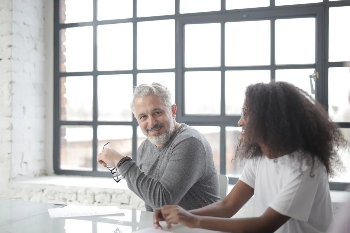 Mentor sênior e jovem estagiária negra sorrindo durante reunião de trabalho