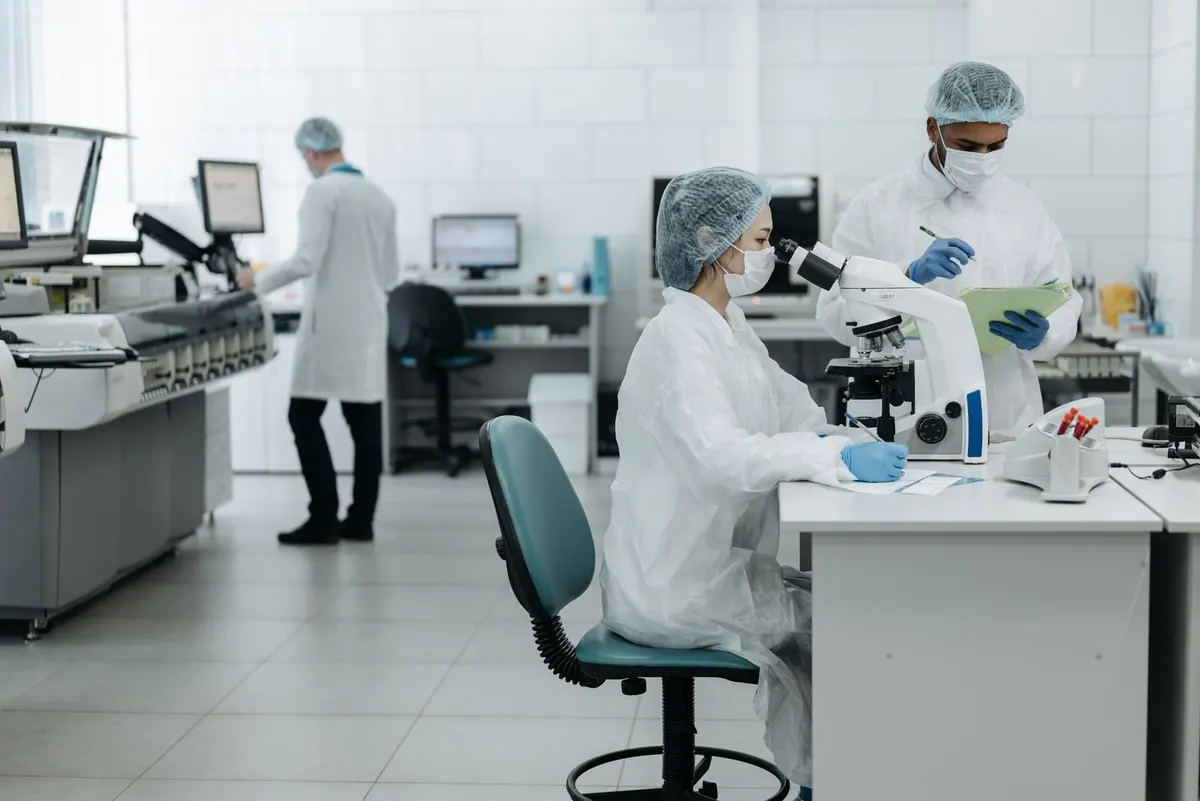 Cientistas em um laboratório moderno, com um ao microscópio e outro anotando.