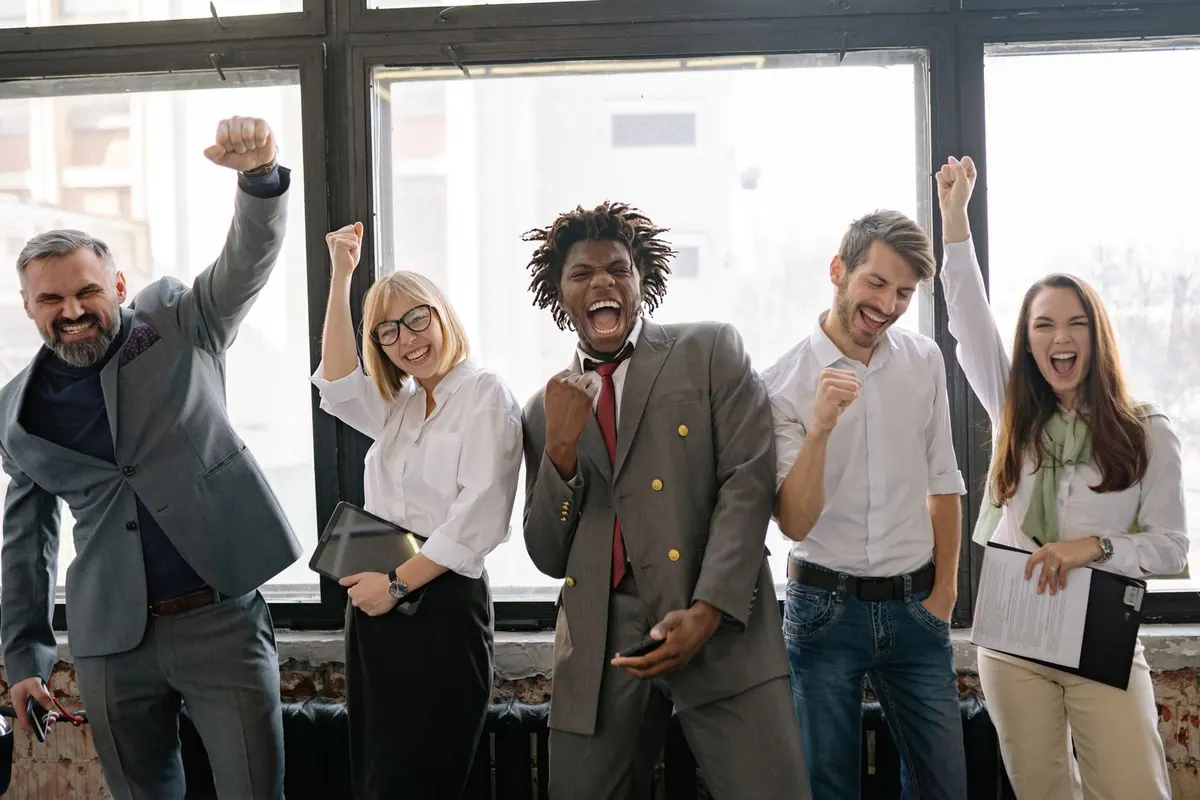 Equipe de escritório diversa e feliz celebrando sucesso com punhos erguidos.
