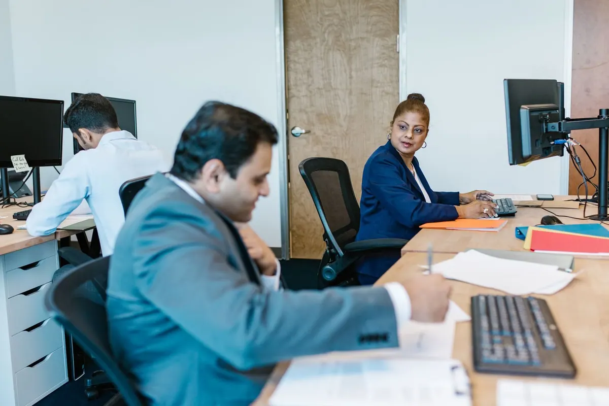 Pessoas trabalhando em um escritório moderno, com foco em uma mulher em frente ao computador.