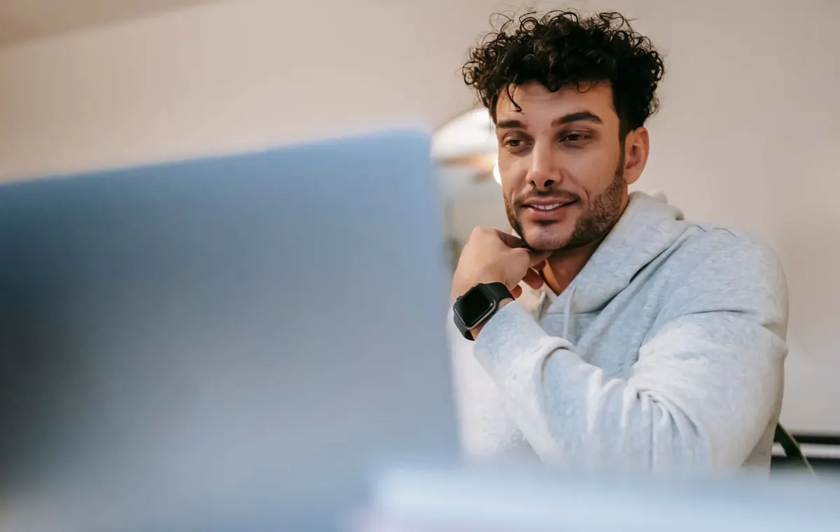 Homem sorrindo assiste a um programa no laptop, representando conexão e engajamento.