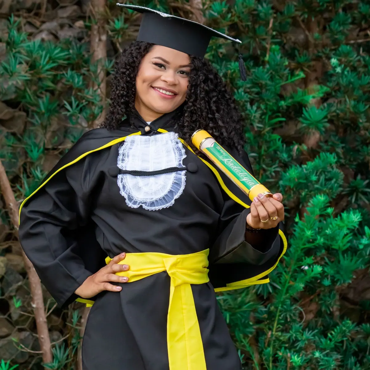 Mulher negra sorridente em beca de formatura segurando um diploma.