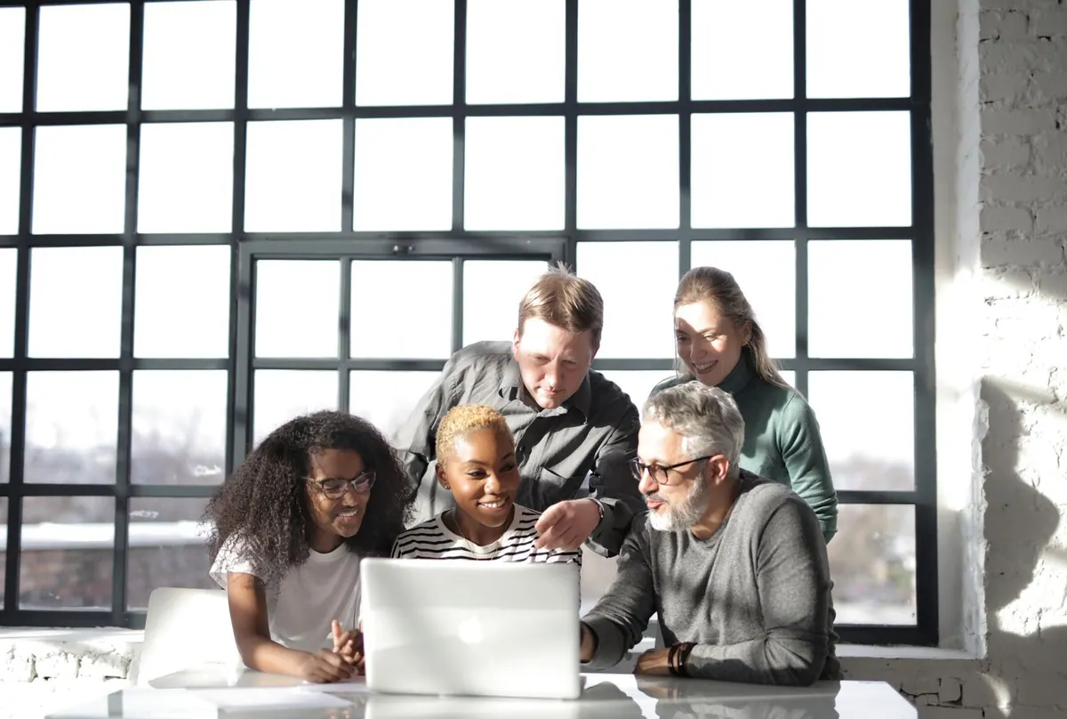 Grupo de colegas de trabalho diversos colaborando em laptop, promovendo aprendizado e desenvolvimento.
