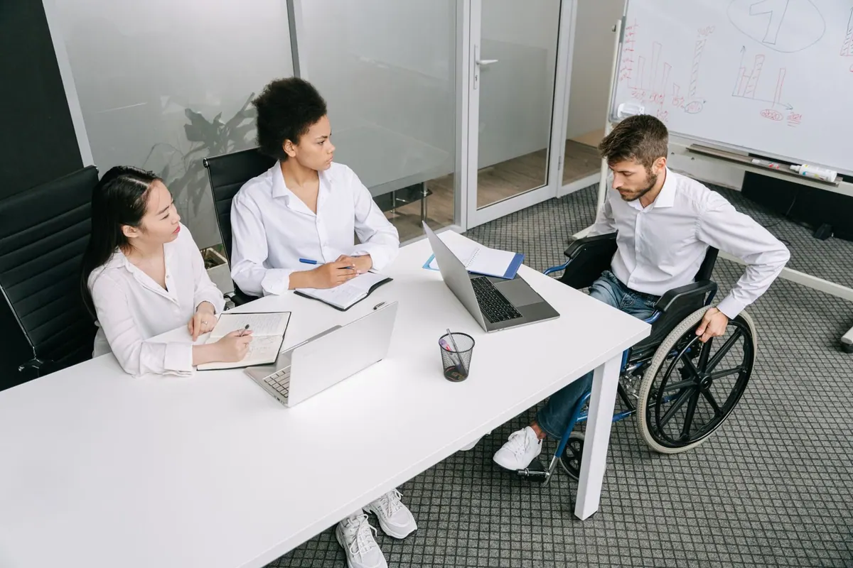 Pessoas diversas em reunião de trabalho, incluindo homem em cadeira de rodas.