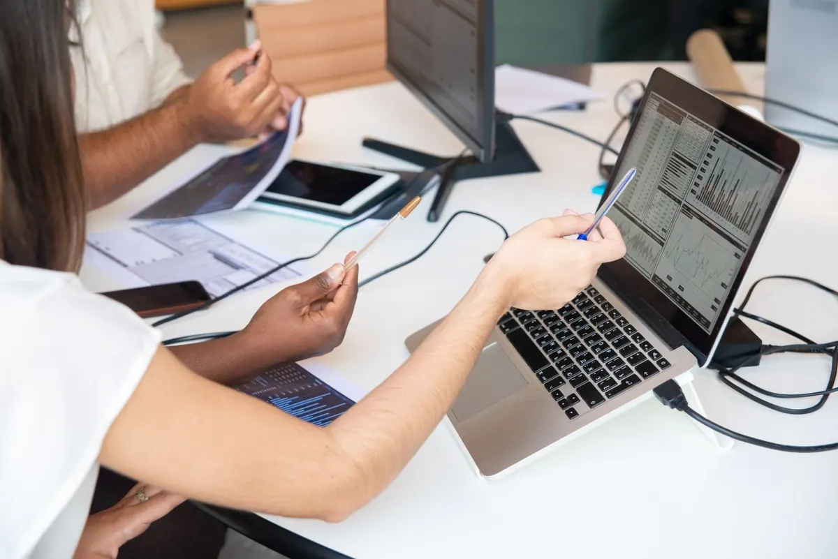 Pessoas analisando dados em um laptop, apontando para gráficos e informações.
