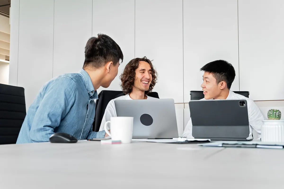 Pessoas em uma reunião de trabalho, conversando e usando laptops.