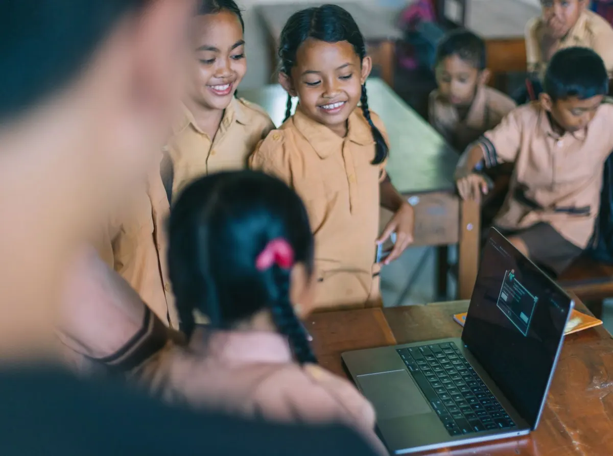Crianças sorrindo enquanto observam um laptop com código de programação.