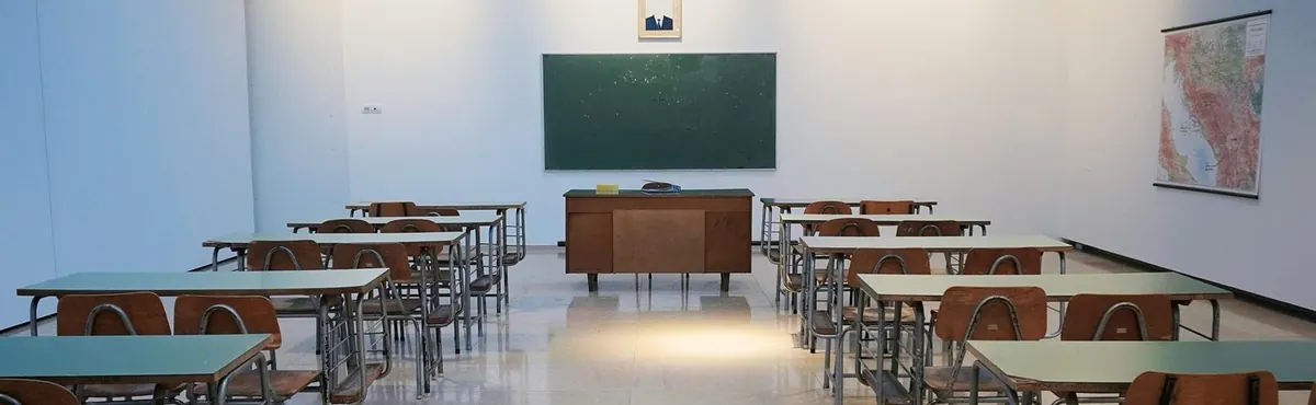 Sala de aula vazia com carteiras e cadeiras enfileiradas, lousa e mapa na parede.