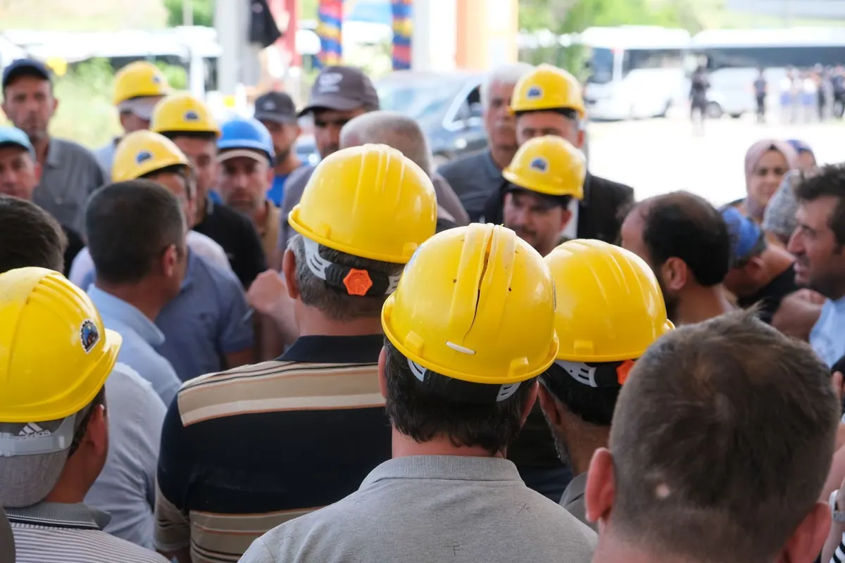 Grupo de trabalhadores com capacetes amarelos reunidos, representando a força de trabalho.