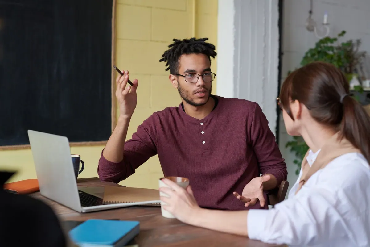 Um homem com dreadlocks e óculos gesticula enquanto conversa com uma mulher.