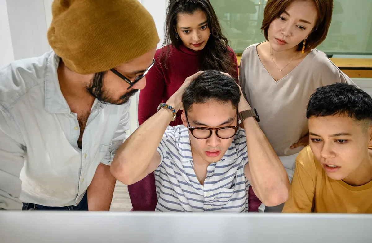 Pessoas jovens e diversas olhando preocupadas para a tela de um computador.