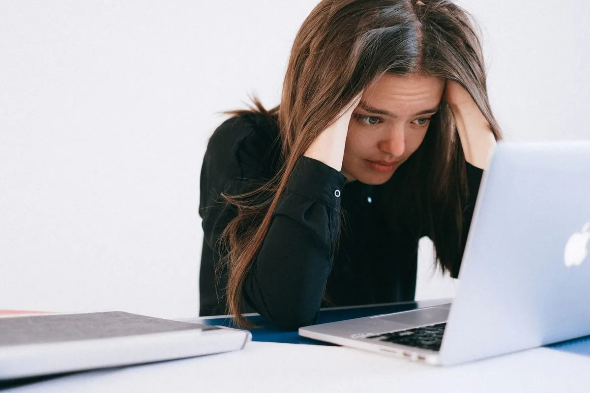 Mulher estressada olhando para um laptop, com as mãos na cabeça.