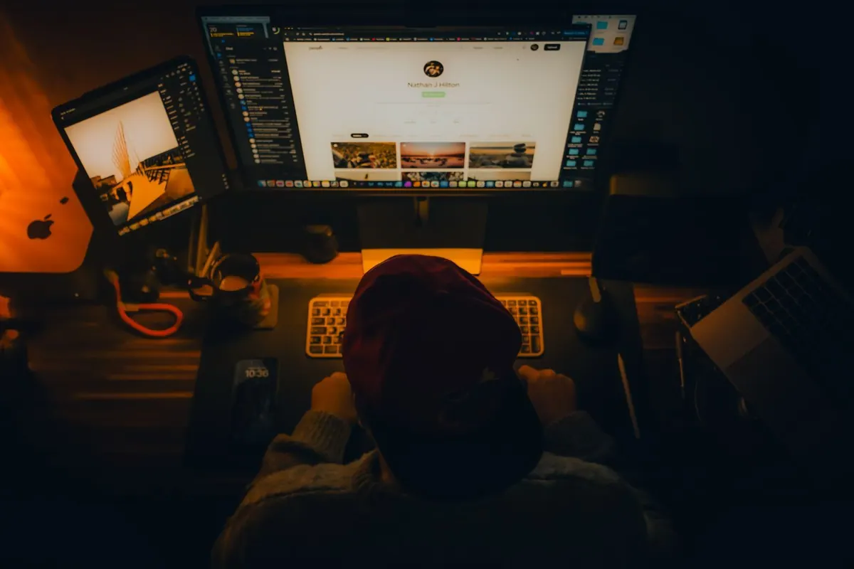 Pessoa trabalhando em um computador com várias telas em um ambiente escuro.