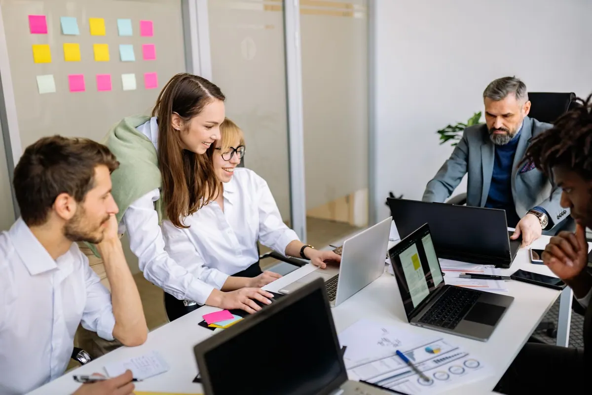 Colegas de trabalho colaborando em uma reunião de escritório, focados em laptops.