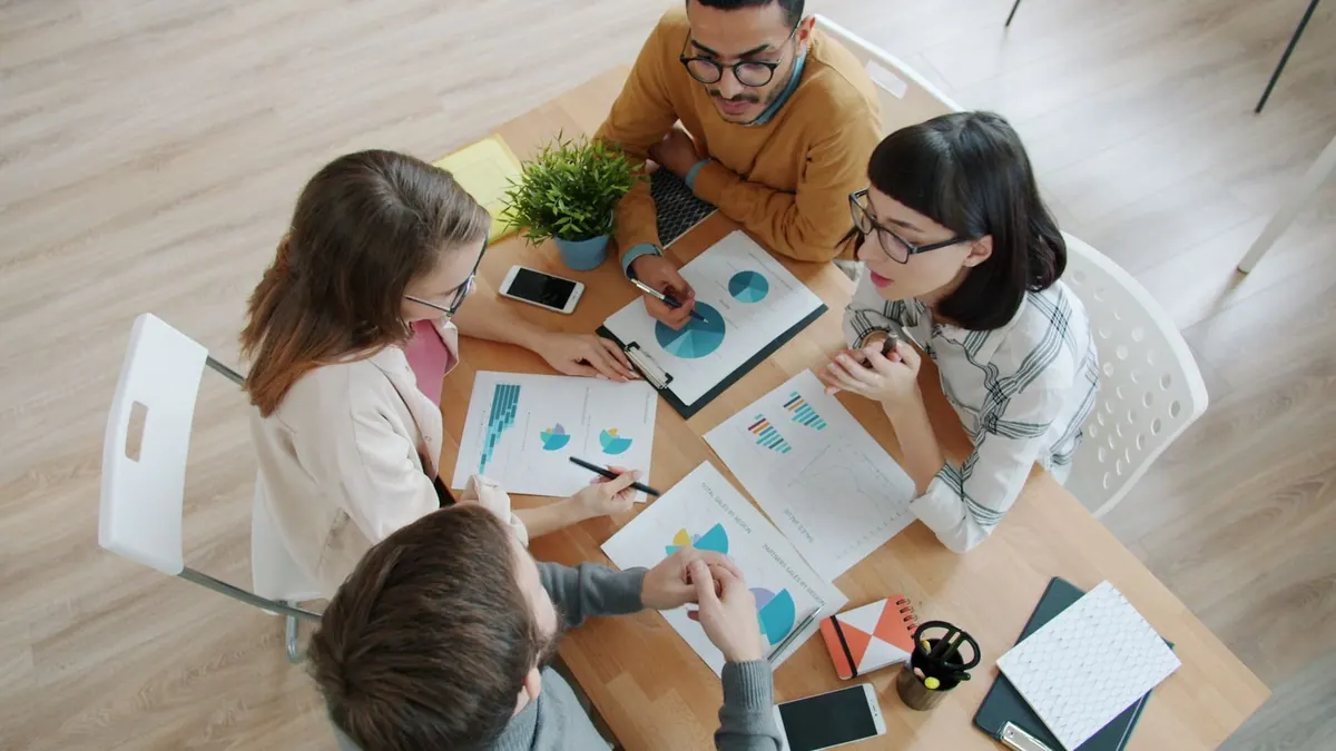 Pessoas diversas trabalhando juntas em uma mesa, analisando gráficos e documentos.